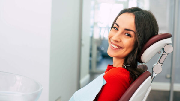 Brown-haired woman leaning back in dental chair with bib on smiling