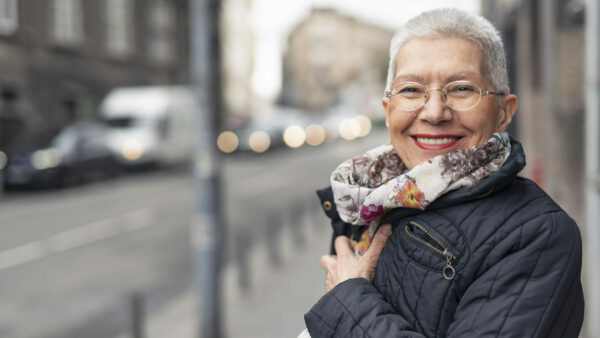 Older woman in jacket and scarf smiling outside Mullins SC Dentist